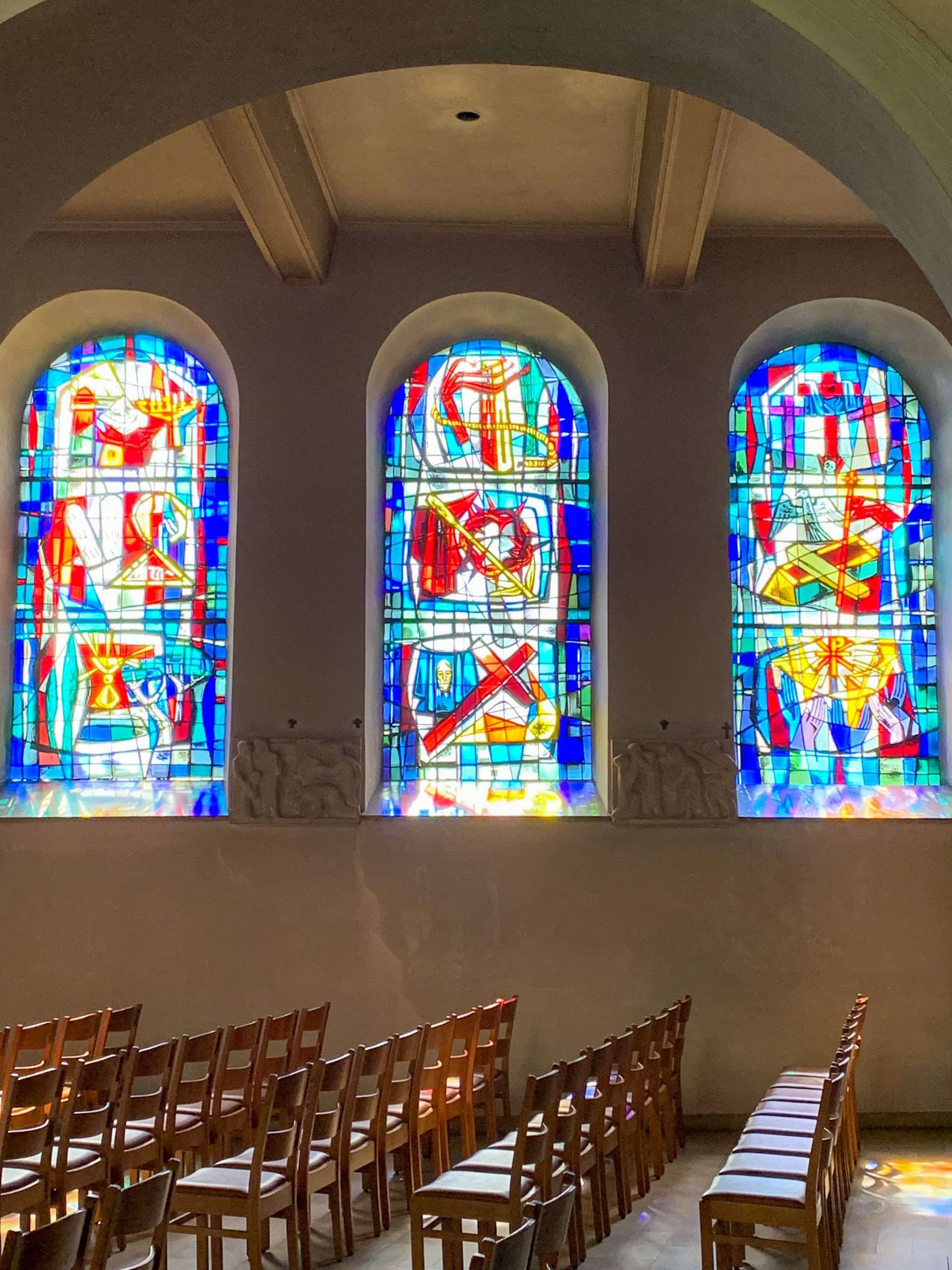 A view of 3 of the stained glass windows inside St Michael's church Luxembourg. Blues and reds dominate the colours of the windows. 