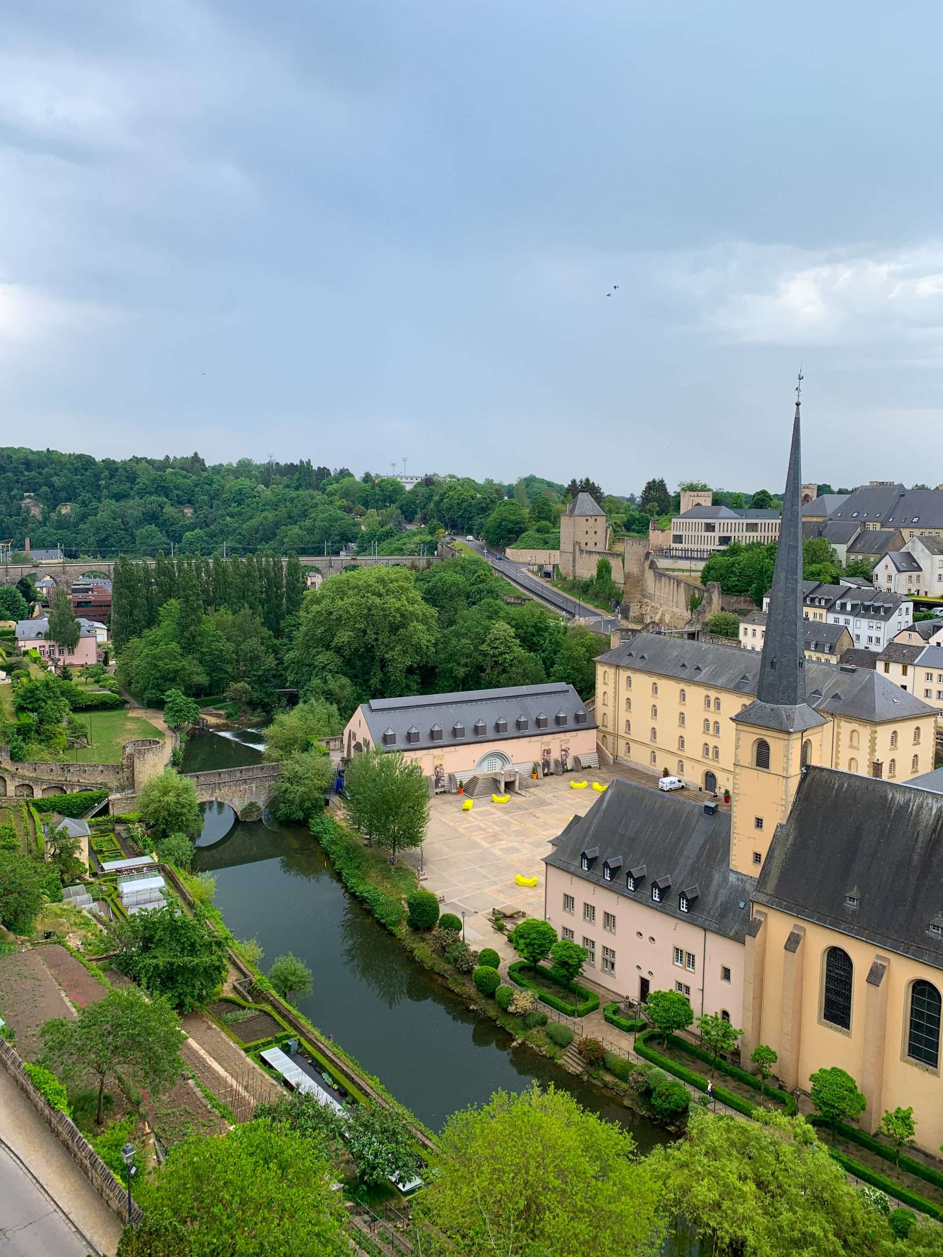 A view overlooking the Corniche and Neimenster cultural centre in Luxembourg with much greenery visible along with the river and surrounding buildings.
