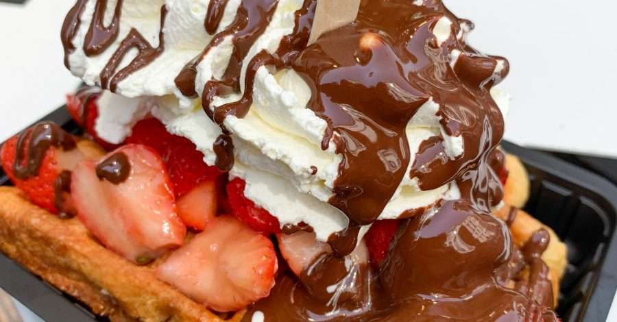 A Belgian waffle with cream and strawberries is covered in melted Belgian chocolate.