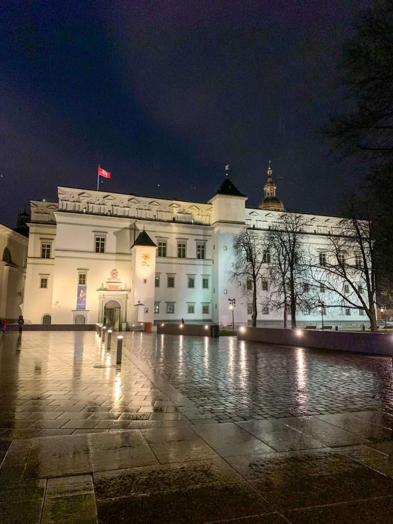 A view of the Palace of the Grand Dukes in Vilnius Lithuania. The image was captured at night with various spotlights shining onto the front of the pale coloured palace.