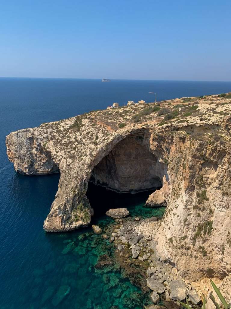 A view of the Blue Grotto in Malta taken from nearby cliffs looking down onto the ocean and rocks forming the grotto.