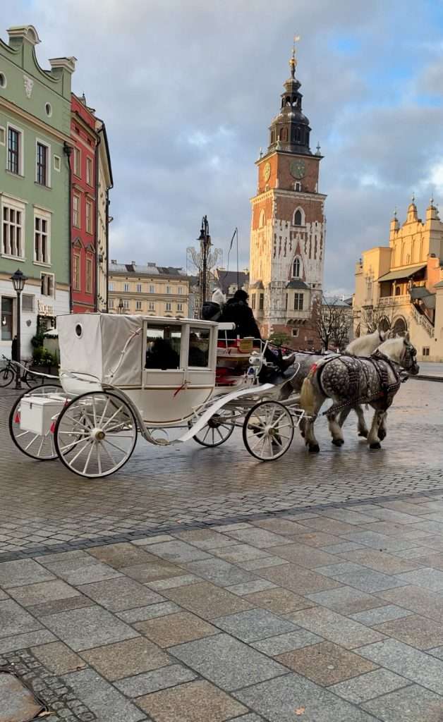 Image shows a horse and carriage in Krakow main square. Amongst the best things to see in Krakow is the huge medieval main market square complete with carriage rides!