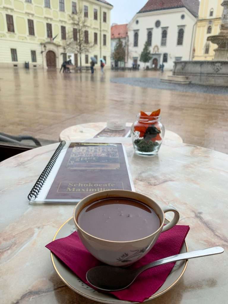Image shows a cup of hot chocolate with Bratislava's Old Town in the background