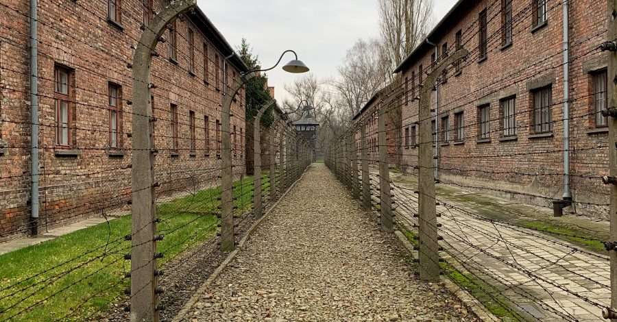 A single gravel path bordered with barbed wire fencing and long dormitory buildings with windows and forming part of the Auschwitz concentration camp near Krakow in Poland.