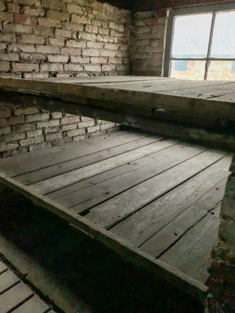 Image shows a reconstructed sleeping platform in the women's barracks at Auschwitz II. Visitors can walk through the barracks during a visit.