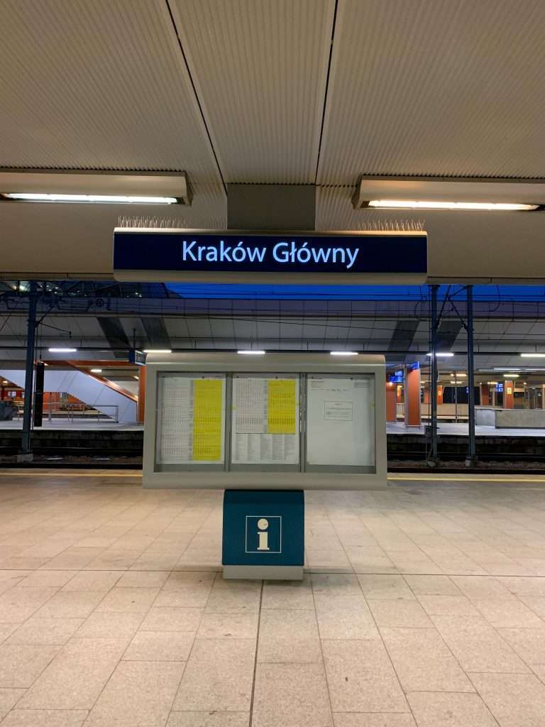 Image shows the sign for Kraków Główny train station, where visitors to Krakow will travel to from the airport