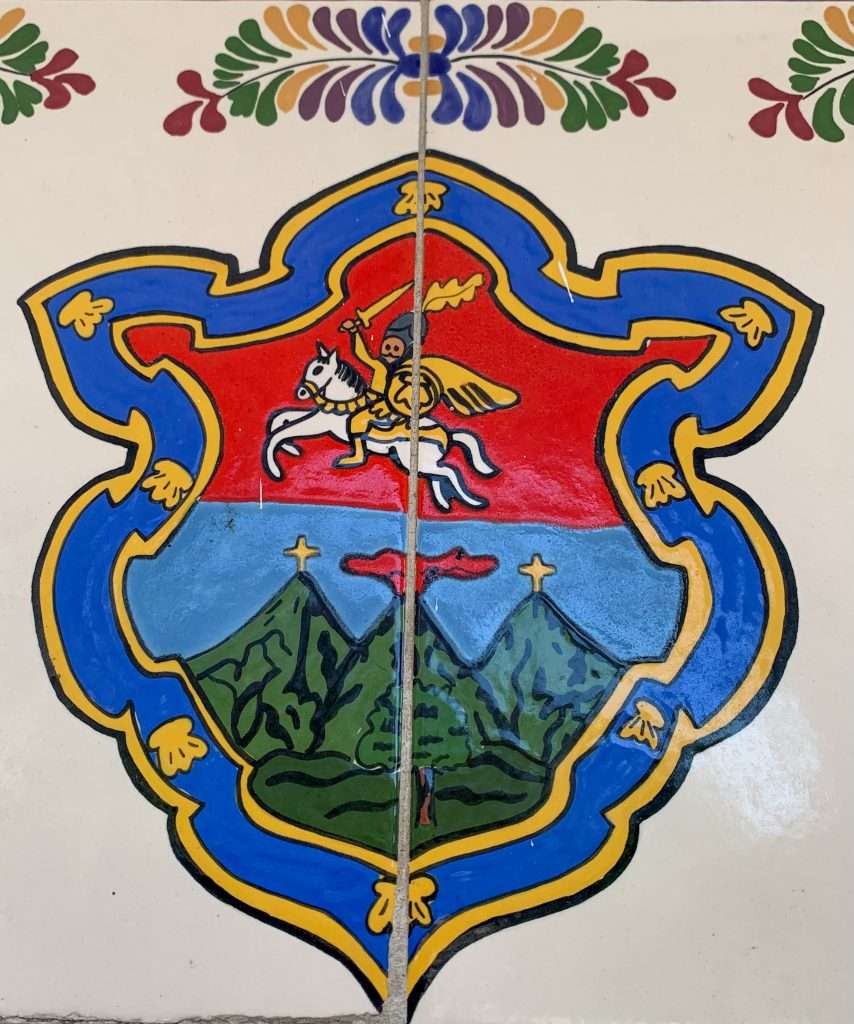 Image shows the Seal of Antigua, a crest featuring, among other images, 3 volcanoes that surround the city of Antigua Guatemala