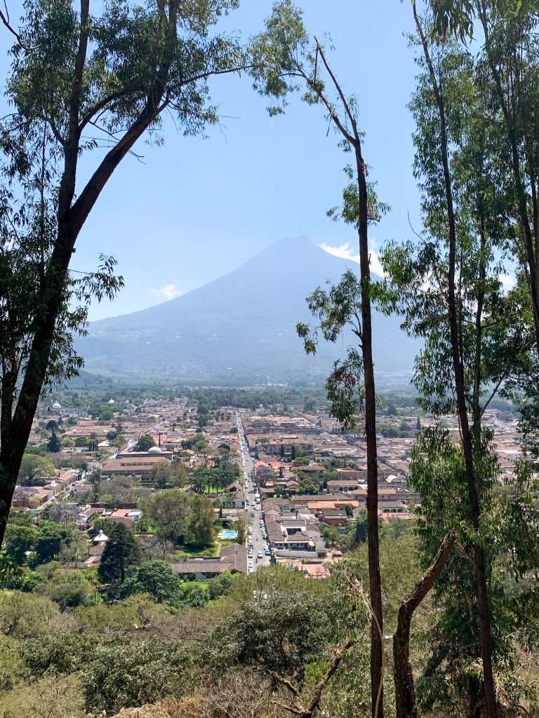Image shows the view of the Agua volcano from the Cross on the Hill with trees and grasses in the foreground. Hiking up to the Cross is one of the best things to do in Antigua Guatemala.