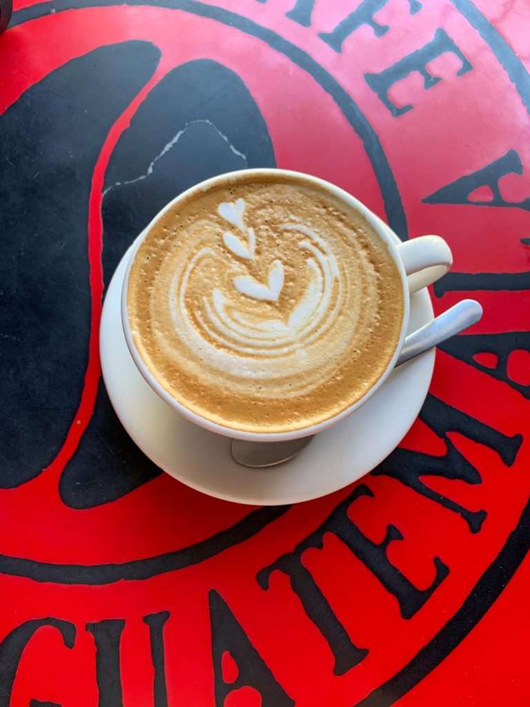 Image shows a cup of coffee against a red and black table. Fueling and refueling with great food and coffee is a must throughout the day in Antigua Guatemala
