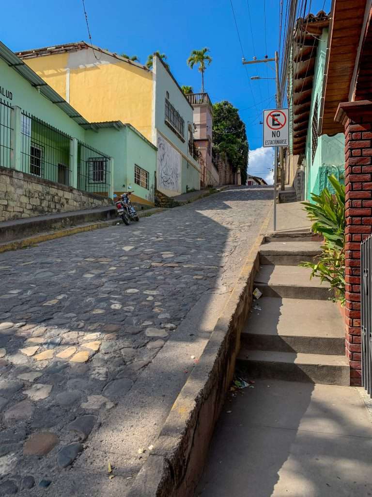 Image shows a view of one of the steep cobbled streets in Copan Ruinas. A great way to explore the streets is by Tuk Tuk. 