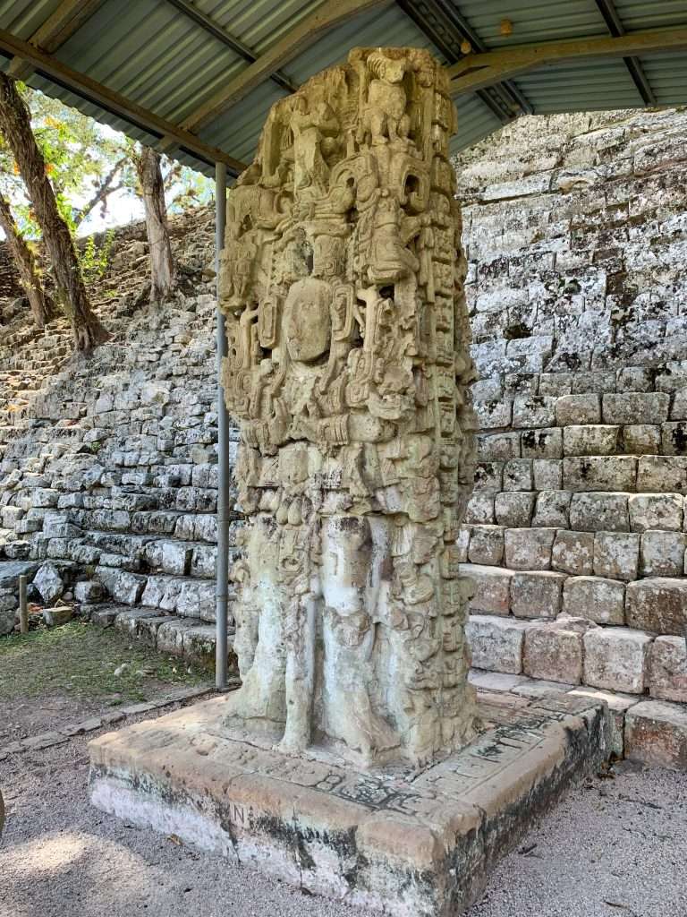Image shows an upright carved block called a stelae as seen at the Mayan ruins of Copan in Honduras, one of the best Mayan ruins to visit