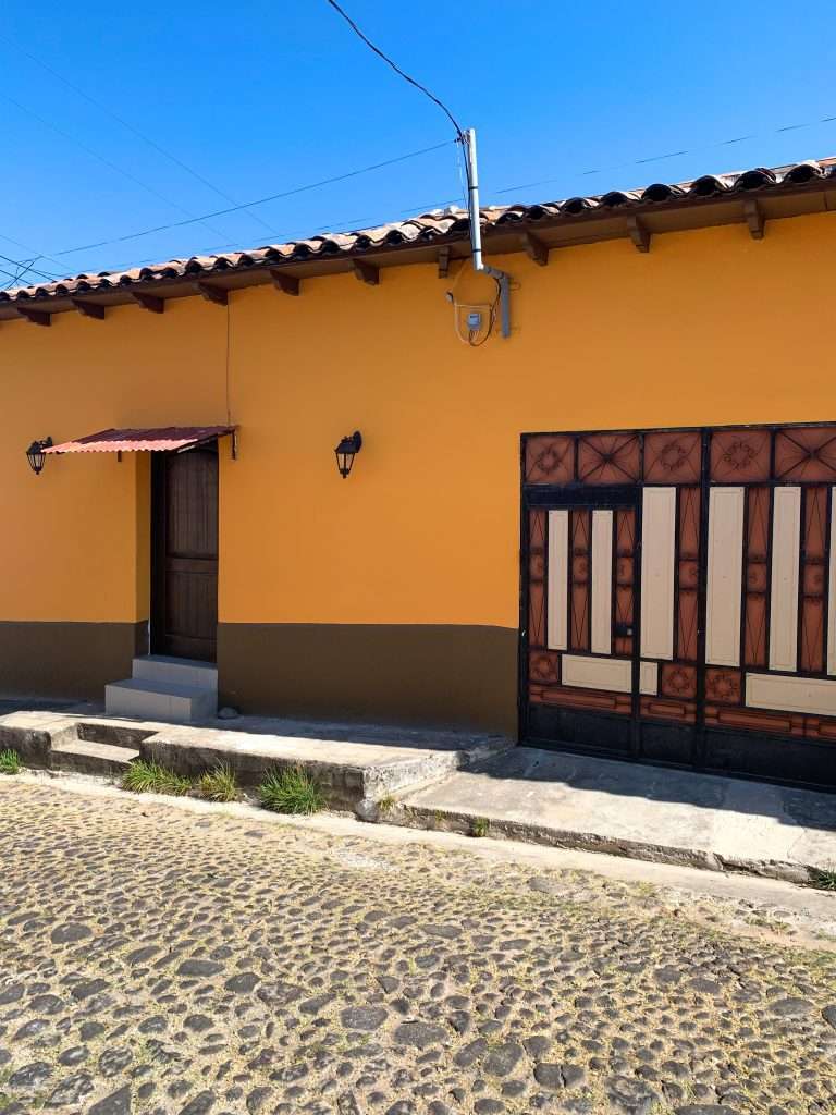 A brightly yellow and brown coloured building with terracotta roof in Suchitoto. Wall lamps are visible as is a decorative wall panel in brown tones.