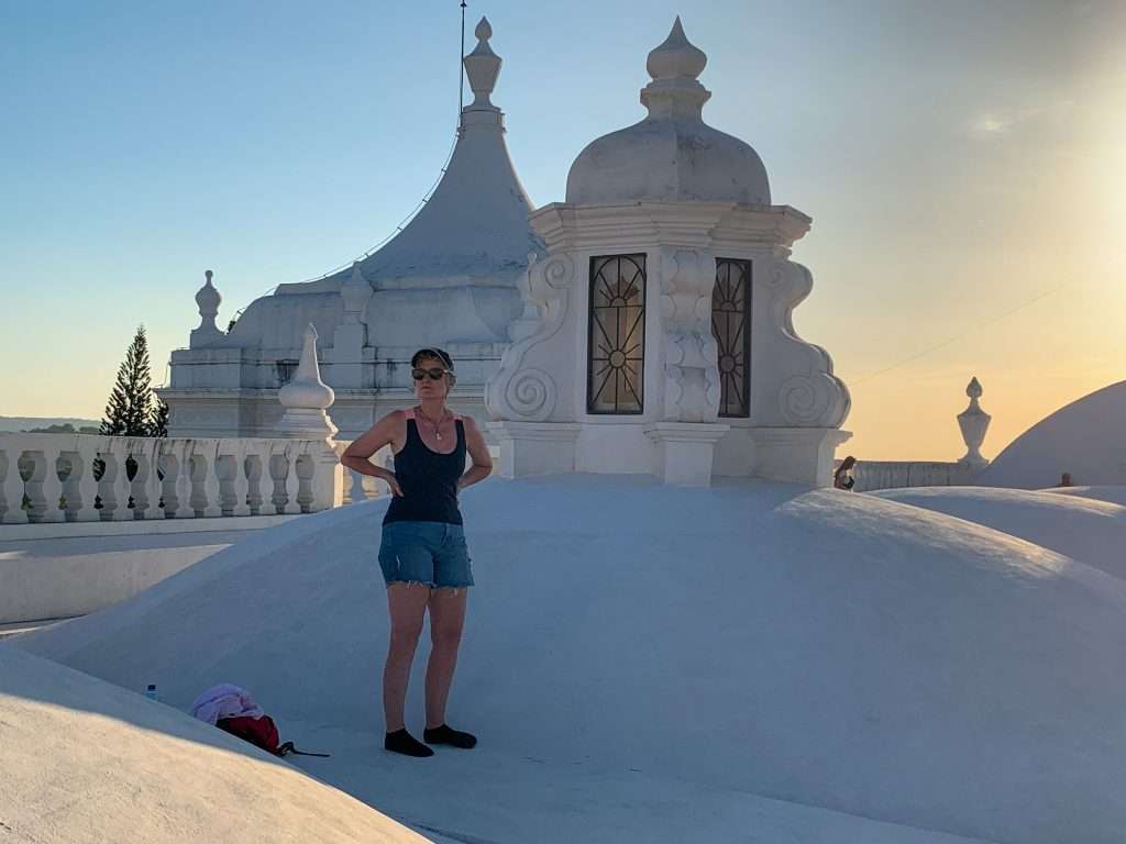 Sarah, the author of this blog post, stands in her socks on the white rooftop of the Leon Cathedral. She wears denim shorts, a navy and singlet with pink coloured straps and sunglasses and a cap.
