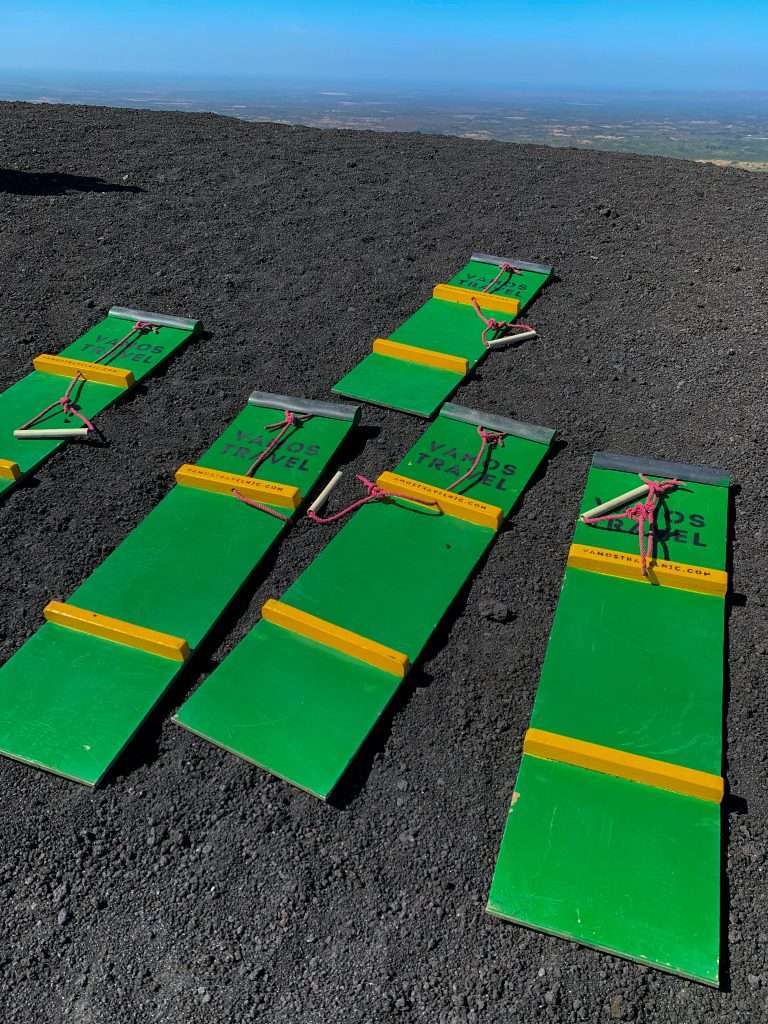 A close up view of the green and yellow coloured plywood boards used for volcano boarding down Cerro Negro volcano in Nicaragua. A red rope with white handle used for holding on is also visible on each board.