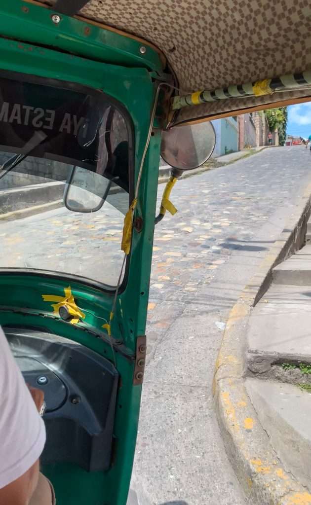 Image shows a view of one of the steep cobbled streets in Copan taken from inside a tuk tuk. 