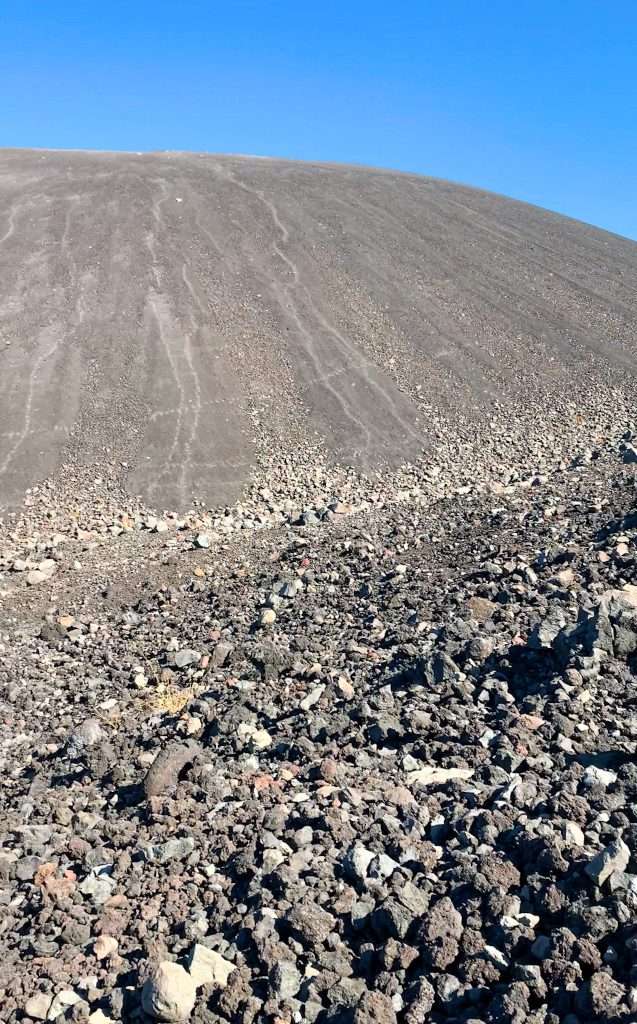 The volcanic rock covering Cerro Negro that those who want to volcano board have to climb. The volcano sits beneath and bright blue cloudless sky.