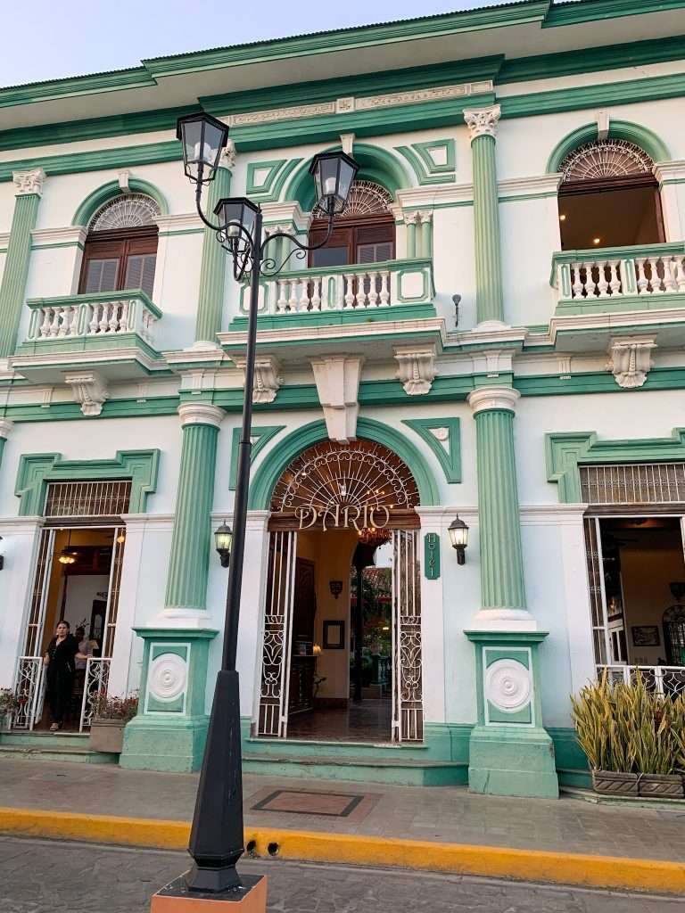 A green and white, ornately decorated colonial era building in Granada Nicaragua. A black lamppost with double lamps is visible in the street outside the building.