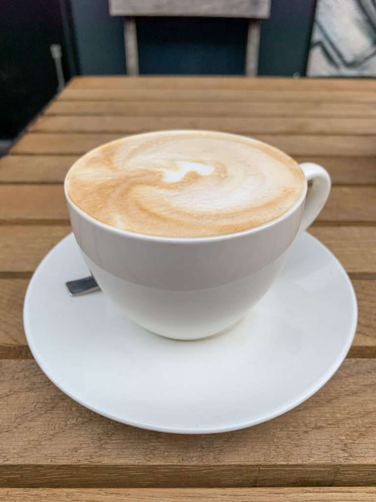 A cup of coffee in a white cup and saucer rests of a wooden outdoor table in Ljubljana.