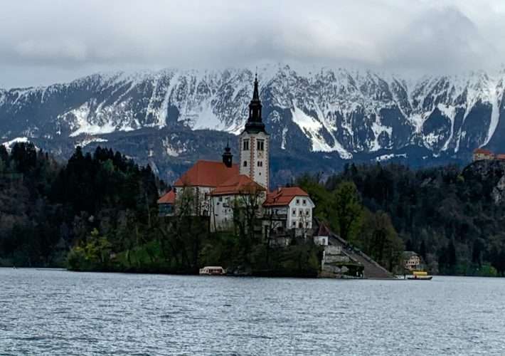 A view looking toward Bled Island on Lake Bled. Snow dusted mountains are visible in the distance.