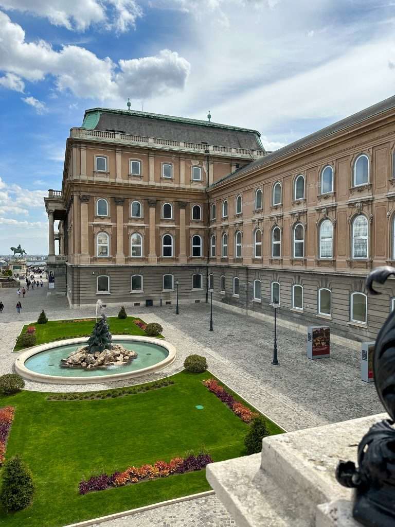 The terrace of the Royal Palace in Budapest, one of its wonderful attractions and definitely worth visiting. A water fountain is visible on a green lawn.