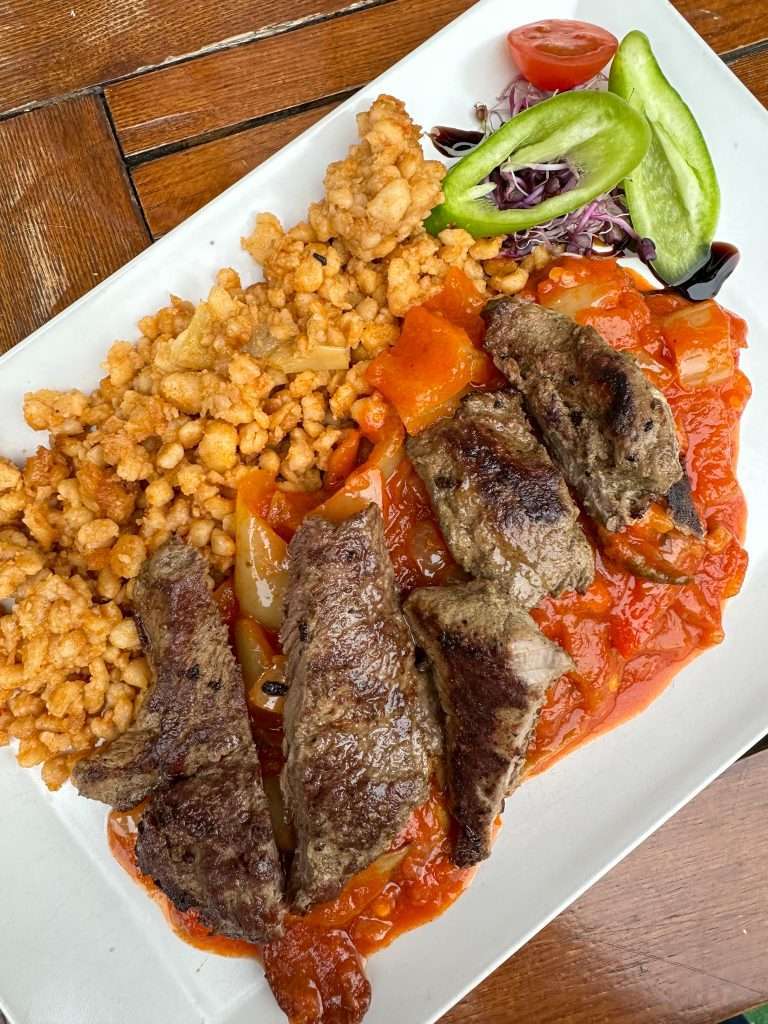 A meal of Hungarian goulash along with some vegetables sits on a white plate. 