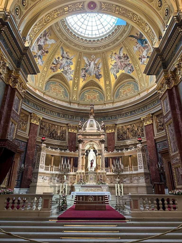 A view of the impressive altar inside St Stephen's Basilica in Budapest. A domed ceiling sits above the altar which is highly decorated with gold and marble. 