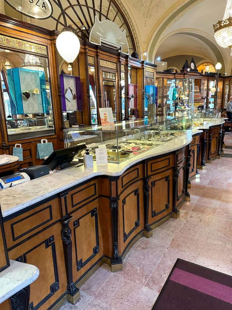 An internal view of Gerbeaud Patisserie in Budapest with the large wooden counter on the left side of the image.