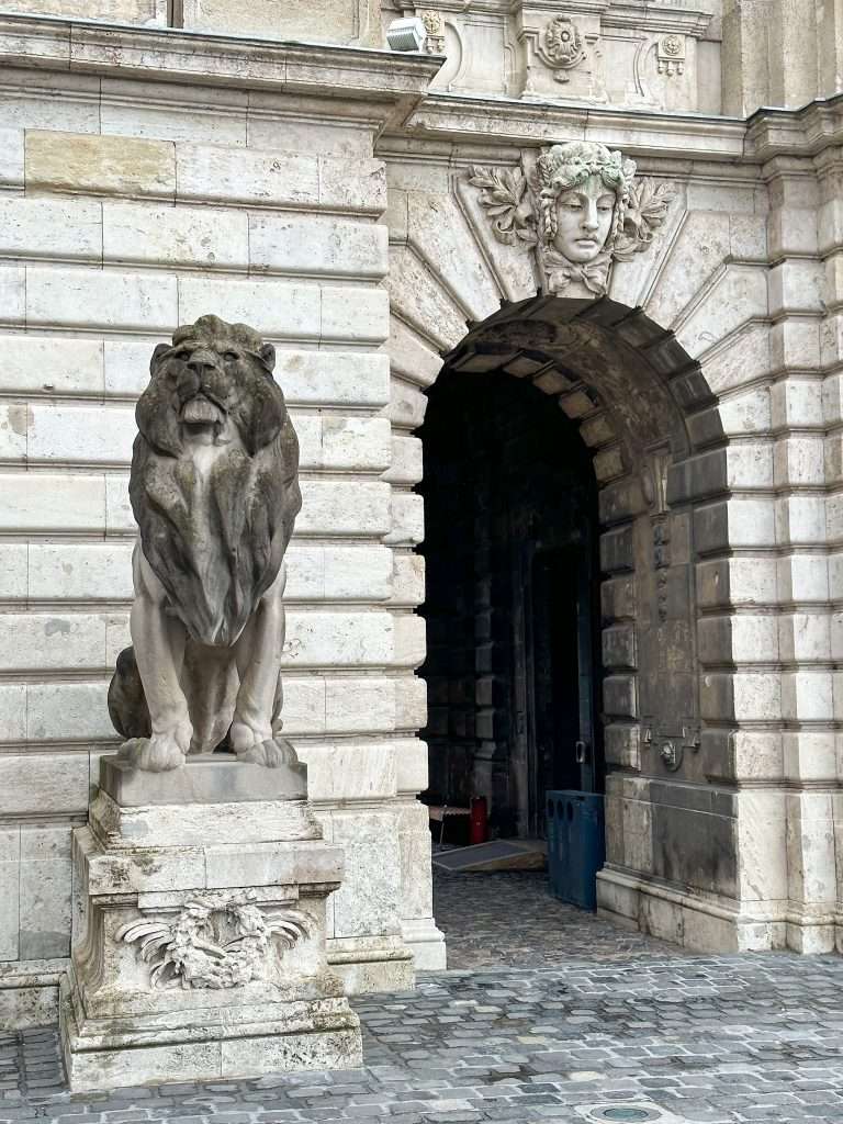 A view of an arched doorway next to which a sculpture of a lion sits on a plinth.