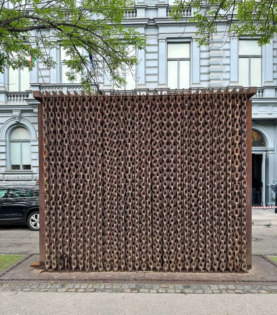 An iron wall sits in front of the House of Terror in Budapest. The wall is in fact a wall of iron chains, an iron curtain, and is a monument to the existence of the wall that divided people and also the eventual victory in tearing it down. 