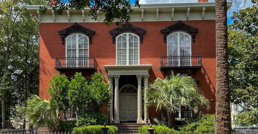 The Mercer Williams House in Savannah Georgia, an impressive red brick house with 3 upstairs windows visible and a portico above the main entrance.