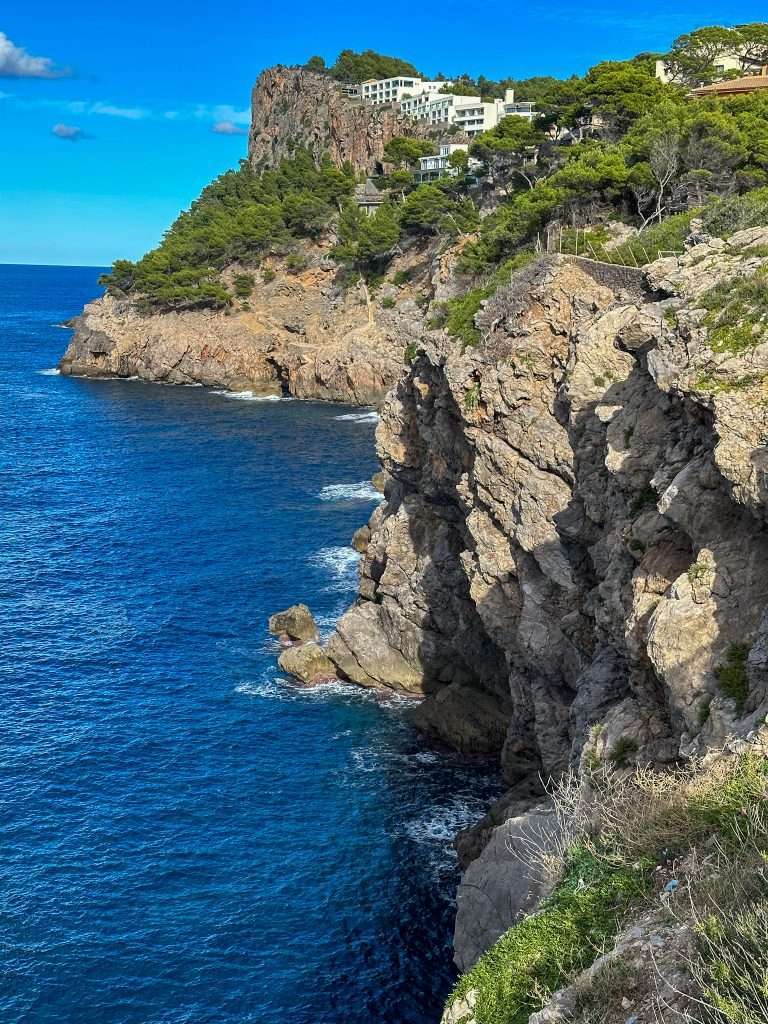 View from the Plaça de Santa Catarina in Port de Soller looking along the coastline with some houses high on a hilltop in the distance.