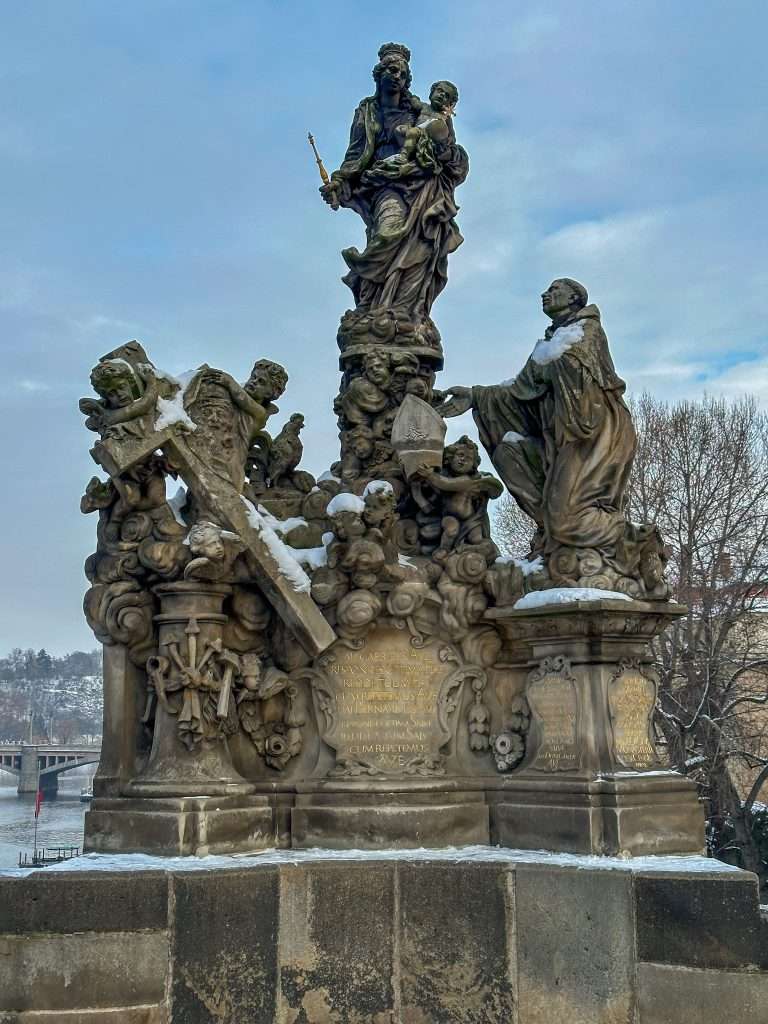 One of the 30 statues on the Charles Bridge, made from stone and featuring various characters. Made from stone it is lightly dusted in snow.