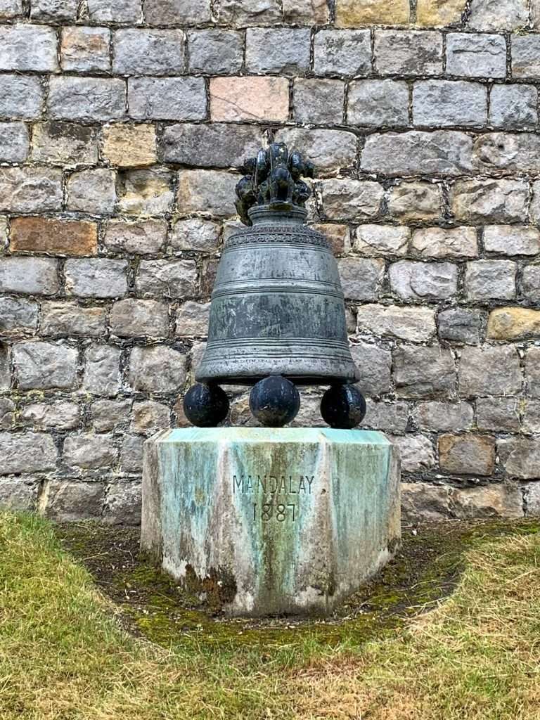 An old bell on a concrete or marble plinth on which is inscribed Mandalay 1887 is located within the grounds of Windsor Castle.