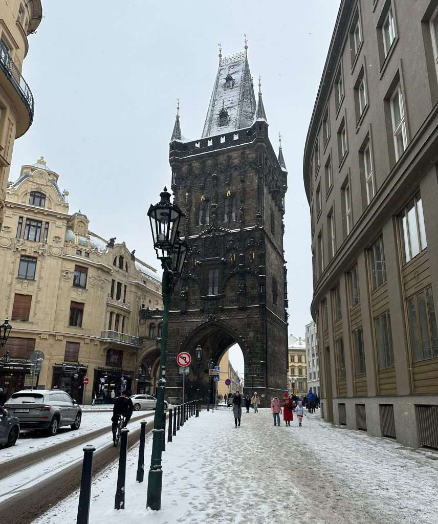 The Powder Gate in Prague seen as part of a walking tour. A 15th century building it's tall with an archway underneath it through which traffic including vehicles travel.