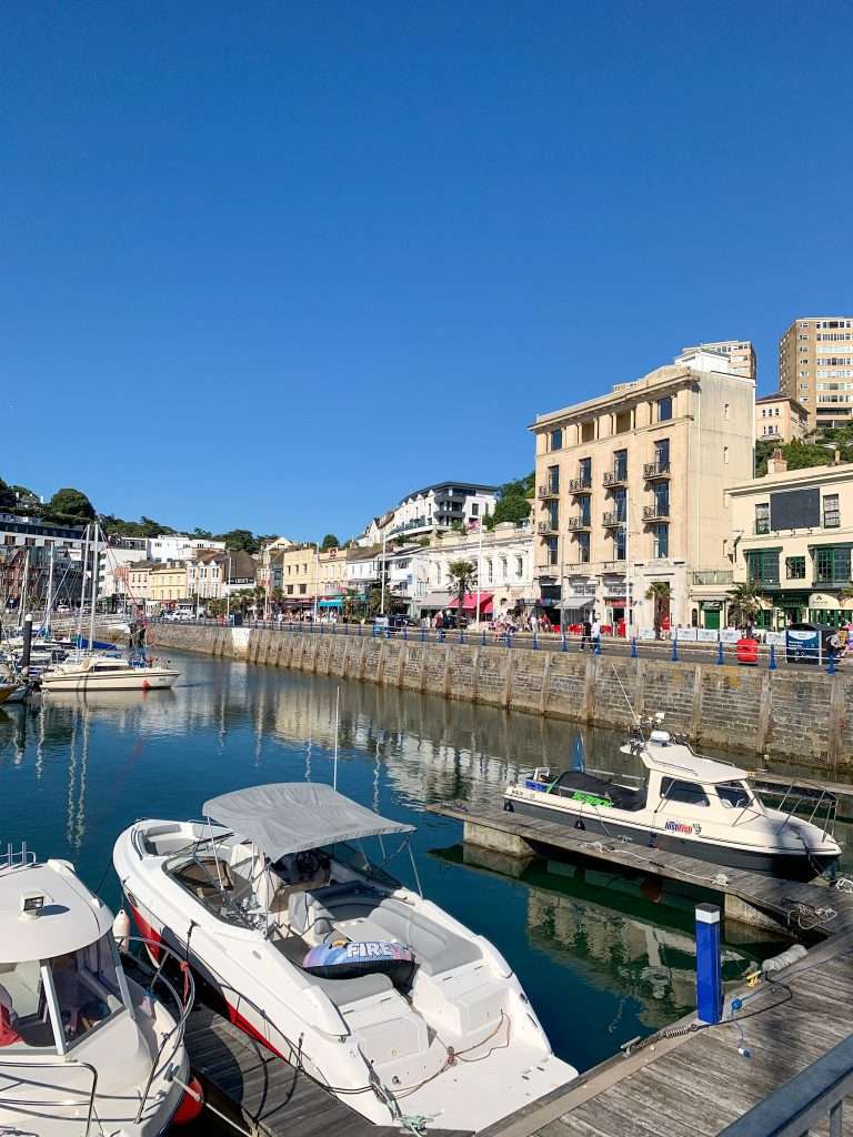 Boats bob gently in Torquay Harbour as the sun sets, casting golden hues—a peaceful highlight of any holiday in Torquay.