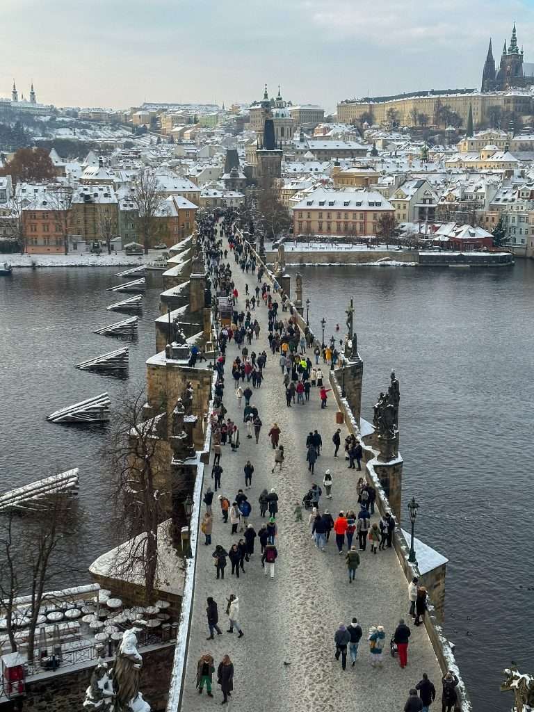 A view over the Charles Bridge in Prague taken from the top of the Old Bridge Tower. Despite the snow on the ground and cold temperatures there are many people crossing the bridge!
