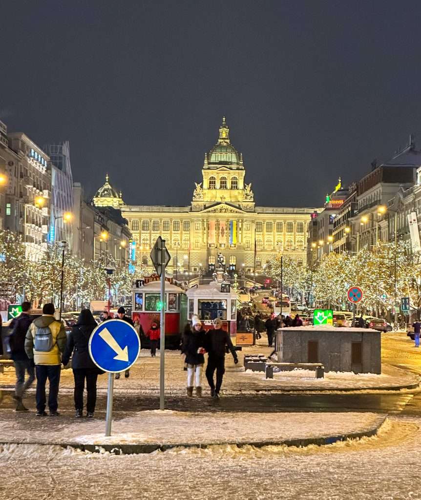 Image shows the Prague Christmas Market in Wenceslas Square. The image was taken at night and shows all the Christmas lights in surrounding trees and buildings