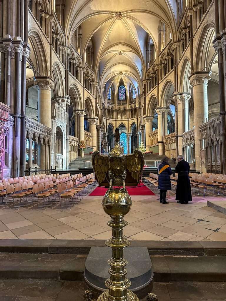 A view inside Canterbury Cathedral looking toward the High Alter. A lectern in the form of an eagle is visible in the foreground as are 2 members of the Cathedral staff.