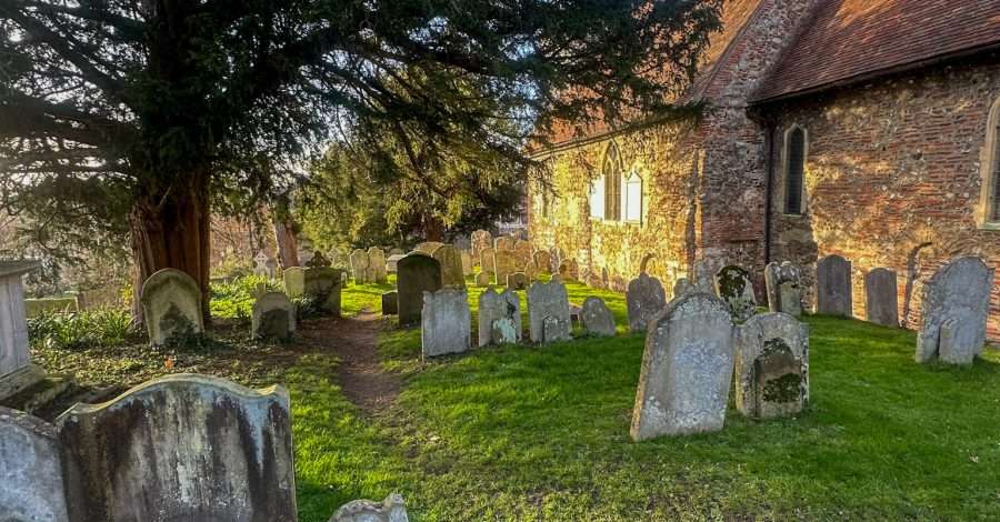 Grave stones located in the Churchyard of St Martin's Church in Canterbury, the oldest church in the English speaking world. A tree grows in the middle of the graveyard underneath a bright blue sky.
