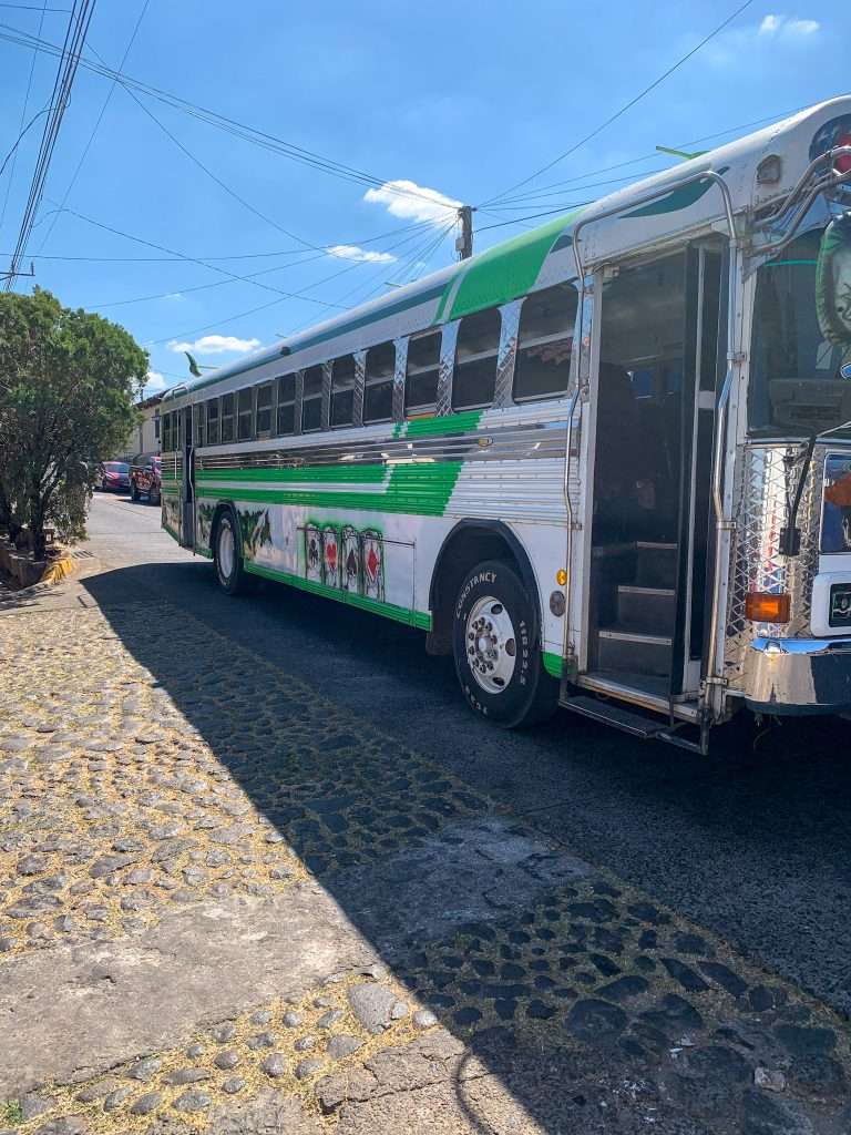 Image shows a green and white bus in Suchitoto, El Salvador stopped along the side of a road.