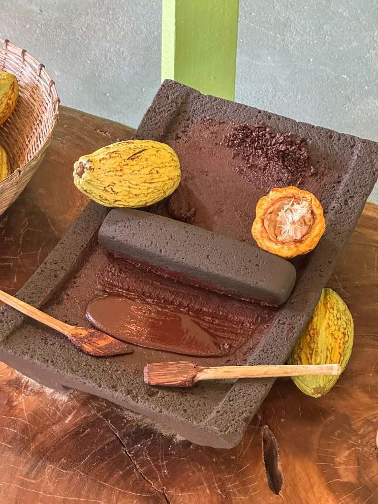 Image shows the traditional Mayan grinding stone with ground cacao beans now forming a paste. Learning about Mayan use of cacao is something to consider including in your Belize travel itinerary.