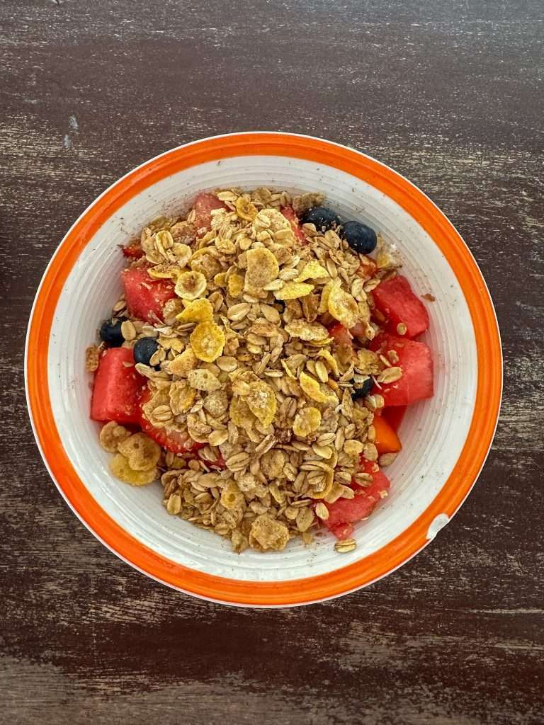 Image shows a white bowl with orange rim filled with cereal and fruit, breast at the Amor Y Cafe in Caye Caulker Belize