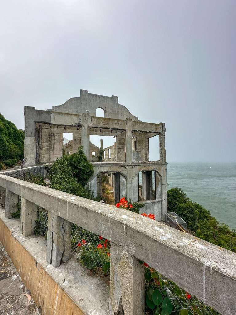 The ruins of the PX and Officers Club located on Alcatraz Island sit amidst some green vegetation and orange coloured flowers.