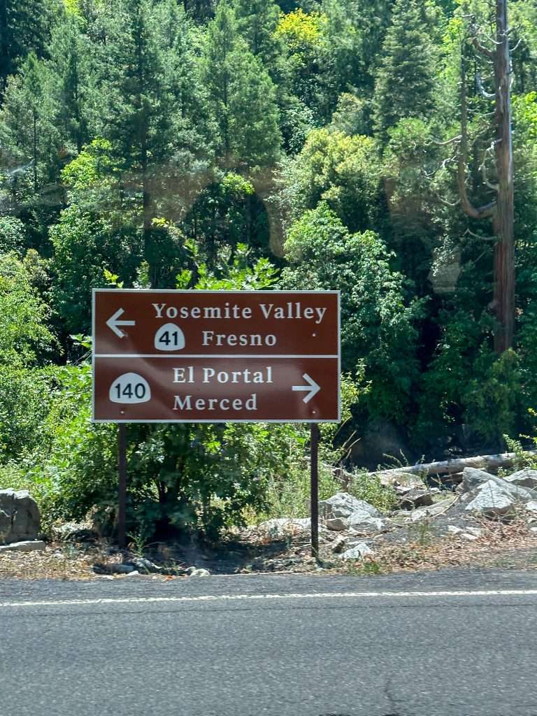 Image is of a road sign pointing out the direction of Yosemite Valley on Highway 41 in one direction and El Portal and Merced in the other direction on Highway 140.