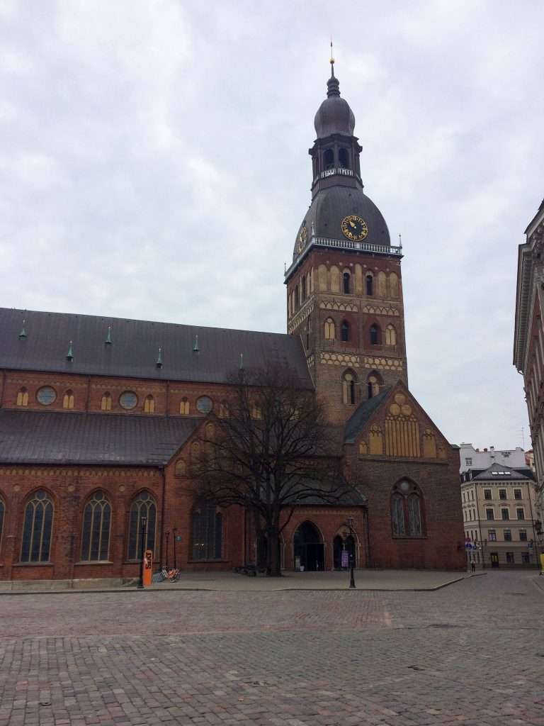 Image shows a view of Riga Cathedral with its tower looming over the adjacent Dome Square.
