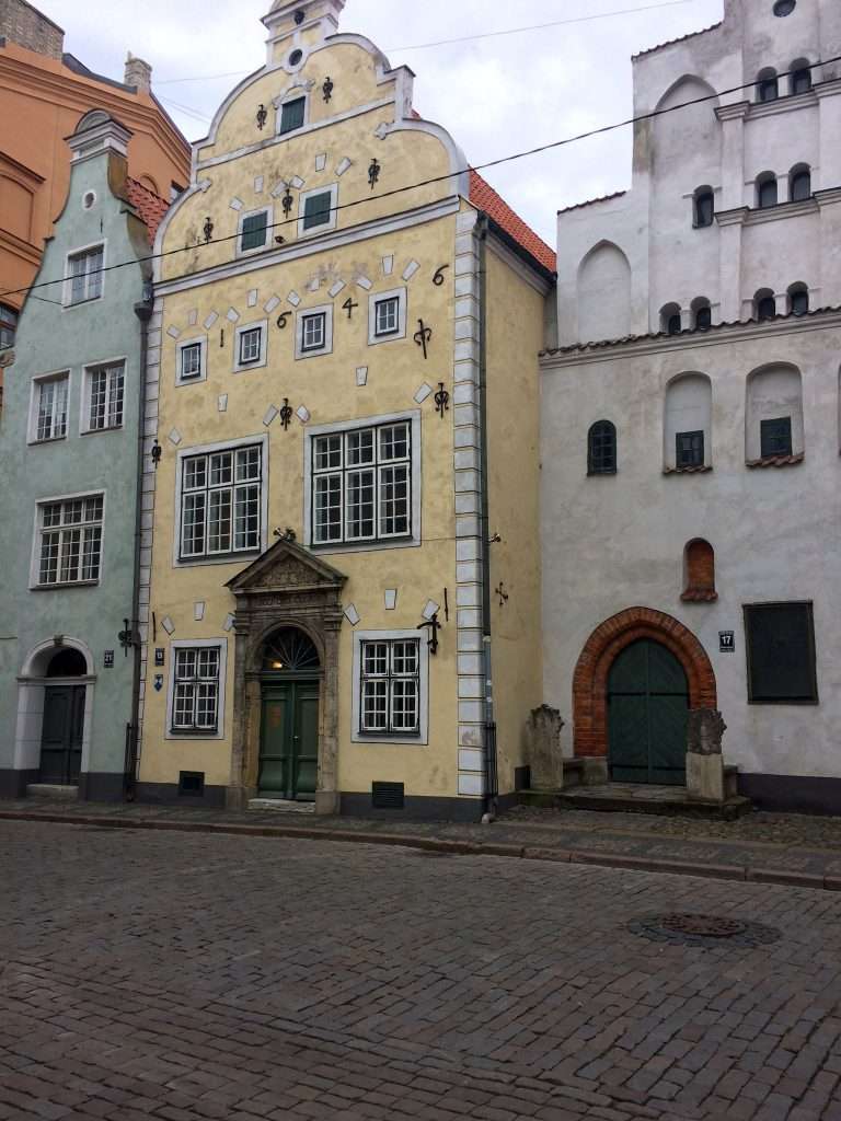 Image shows the Three Brothers in Riga, a line of the oldest houses in Riga. From left to right the houses are coloured a pale green, yellow and a cream.