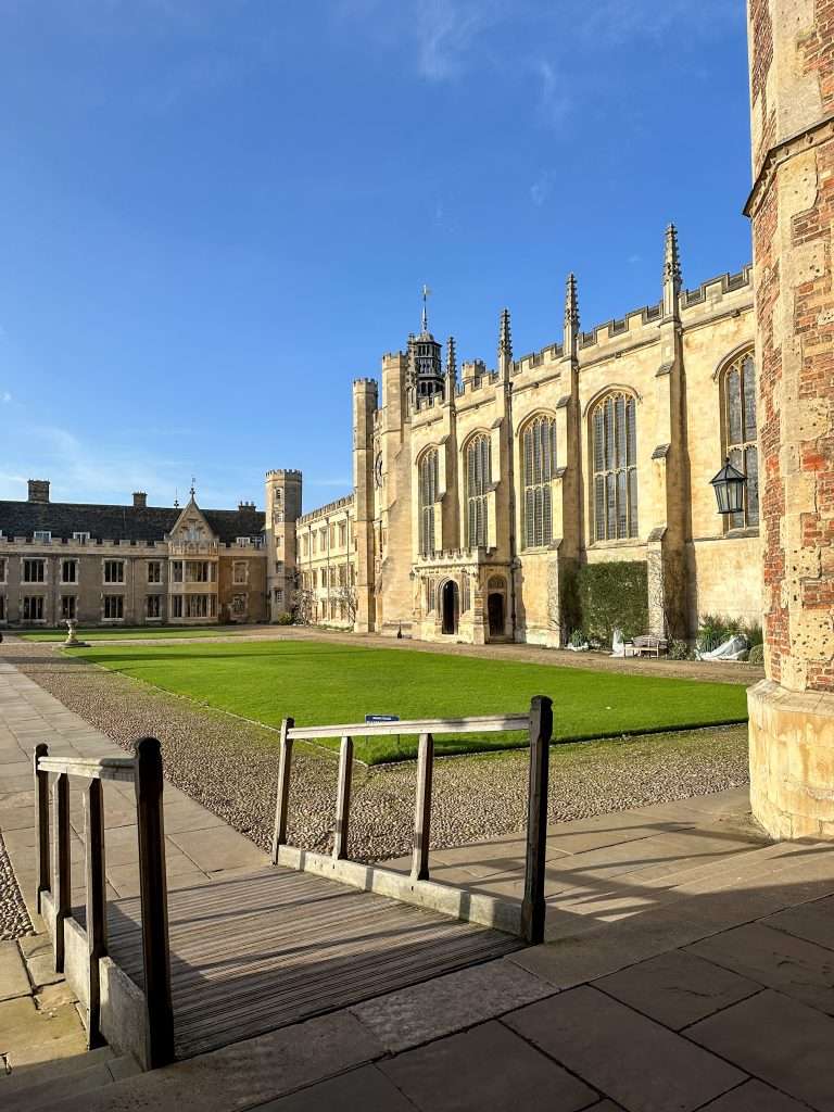View of a large grassed courtyard at Trinity College, part of Cambridge University. There is a wooden ramp in the foreground allowing for accessibility.