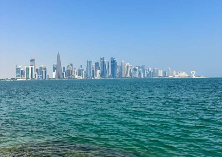 The Doha skyline looking across the sea. Various tall buildings are visible, including one that is a tall pyramid like shape.