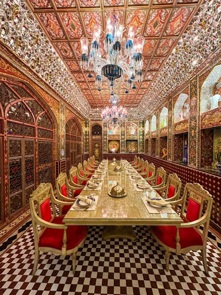 An incredibly ornate private dining room within the Parisa restaurant. Red chairs surround a long dining table set with ornate plates and cutlery with the walls and ceiling encrusted with crystals and glass.