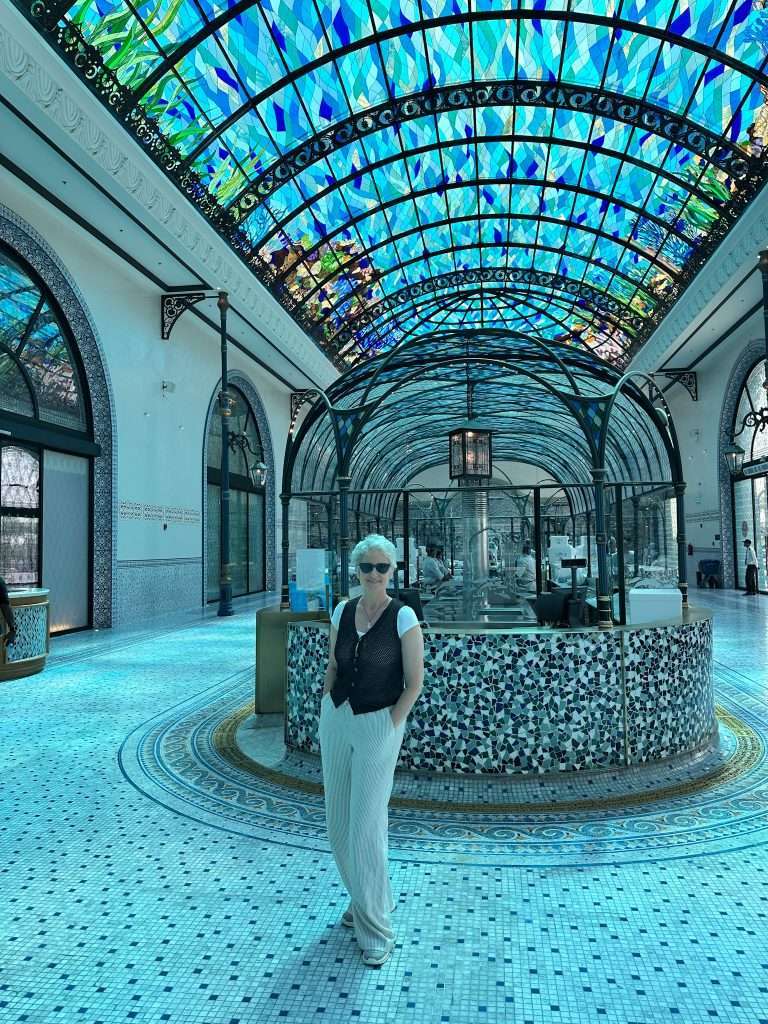 Sarah, the author of this blog post in the fish market in Doha wearing long, loose fitting linen trousers, comfortable walking shoes, a brown cotton woven waistcoat with white t-shirt underneath and sun glasses.